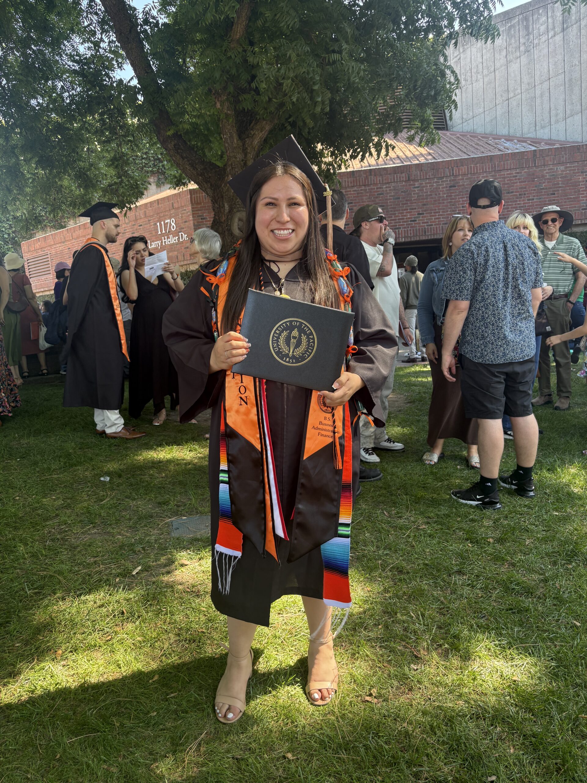 Alondra Duran in graduation regalia holding her decorated cap outdoors on graduation day