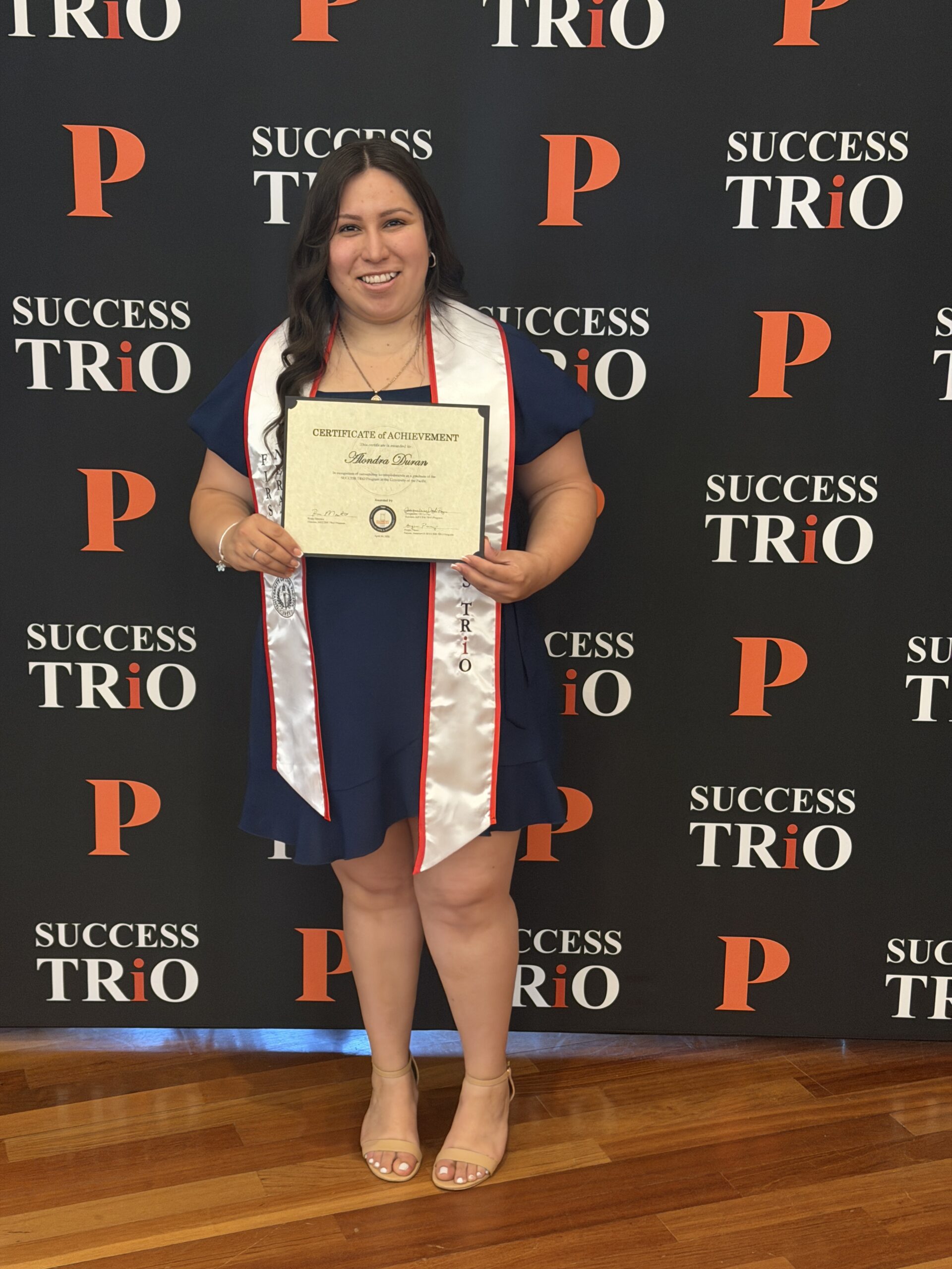 Alondra Duran holding a certificate in front of a Success Trio backdrop