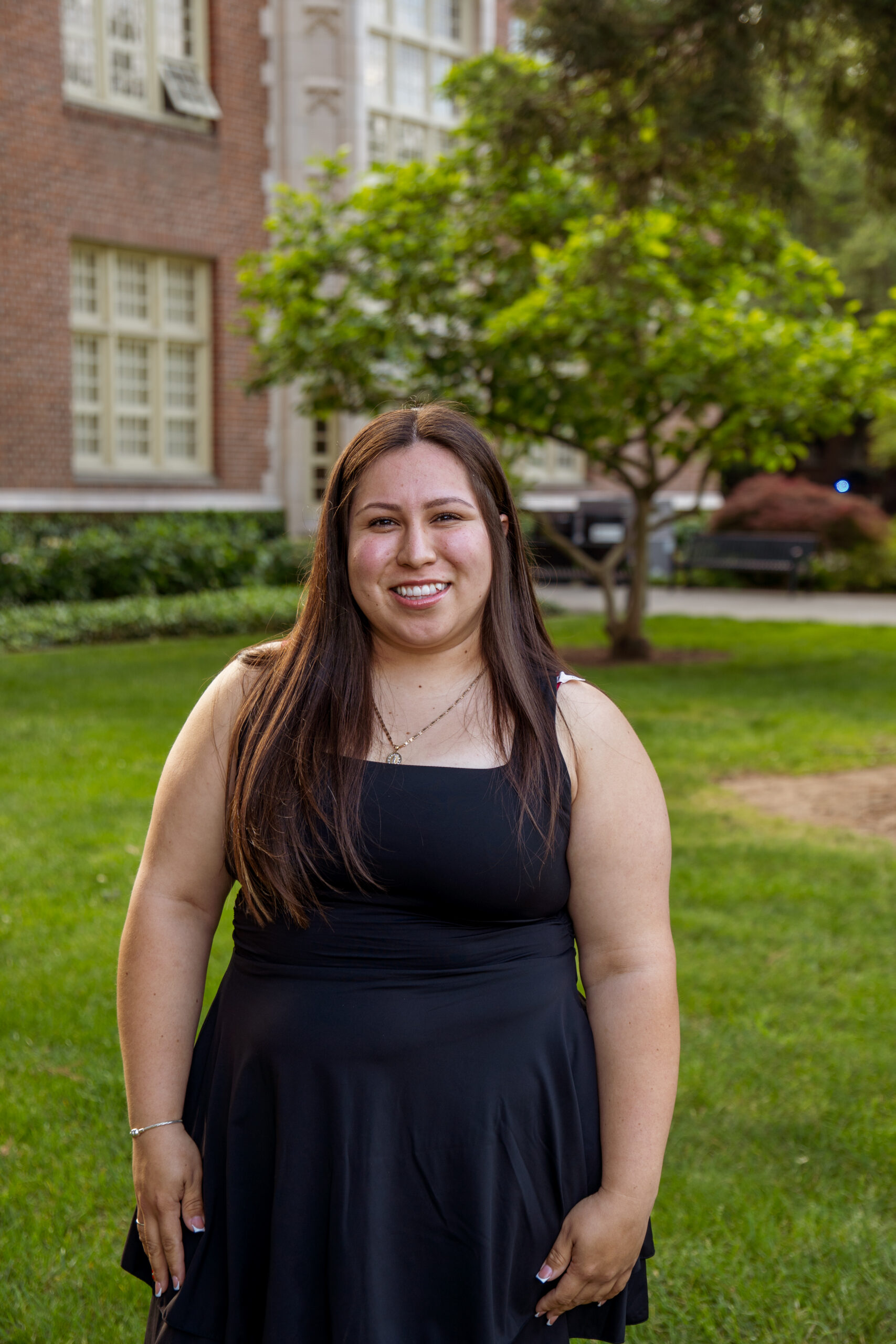 Alondra smiling outdoors in front of a campus lawn and brick building