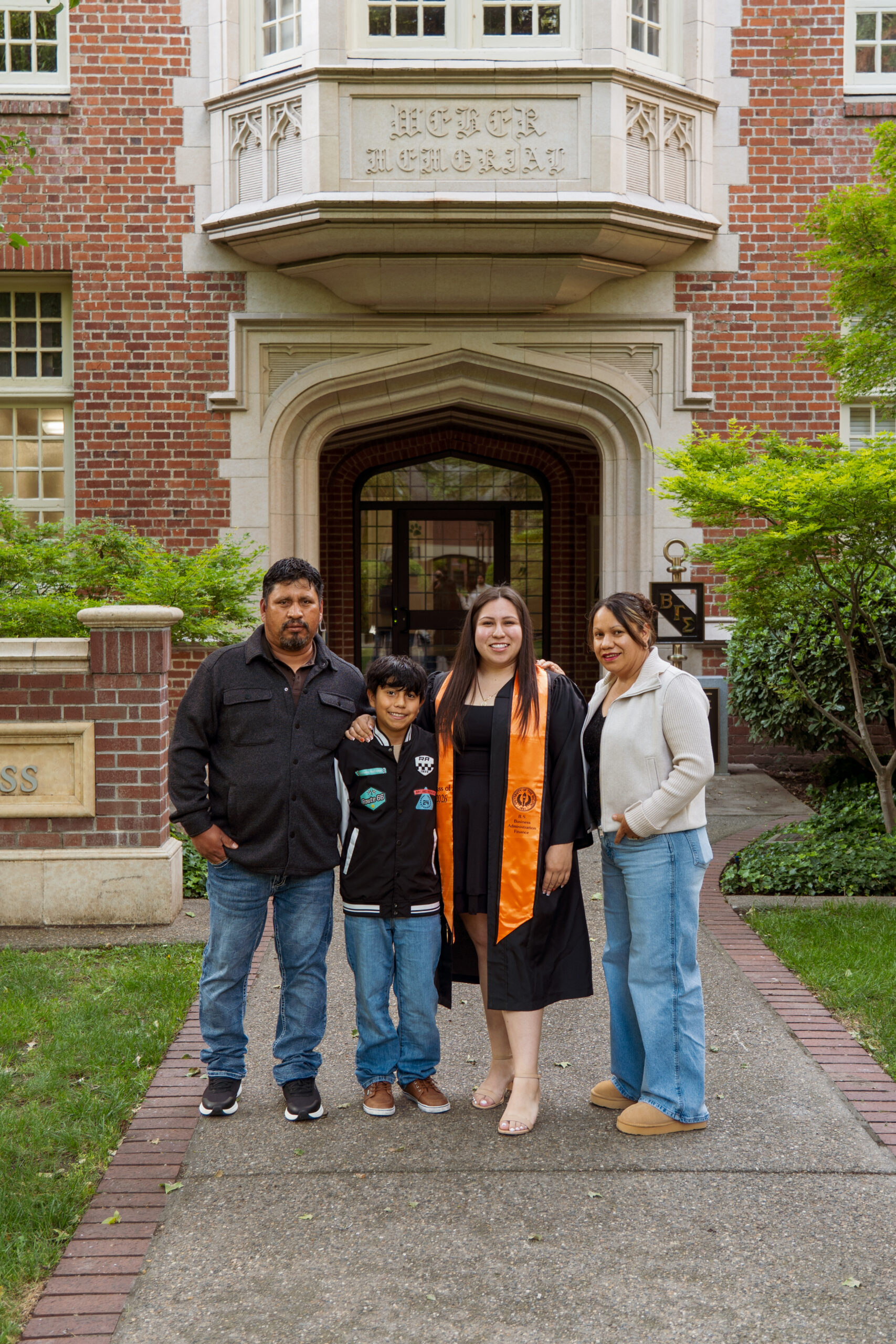 Alondra with family in front of a campus building entrance on graduation day